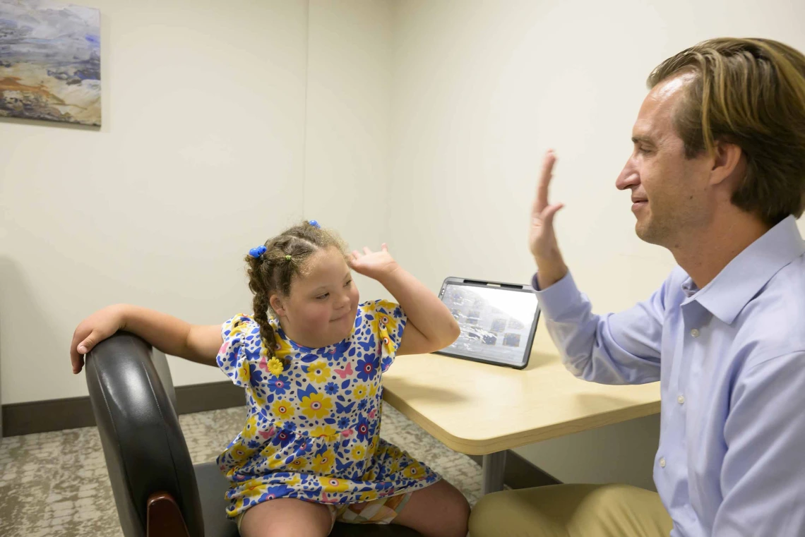 Dan Combs, MD, assistant professor in pediatrics and sleep medicine at the University of Arizona College of Medicine – Tucson’s Department of Medicine, holds his hand up to a young Down syndrome patient for a high five in an office.