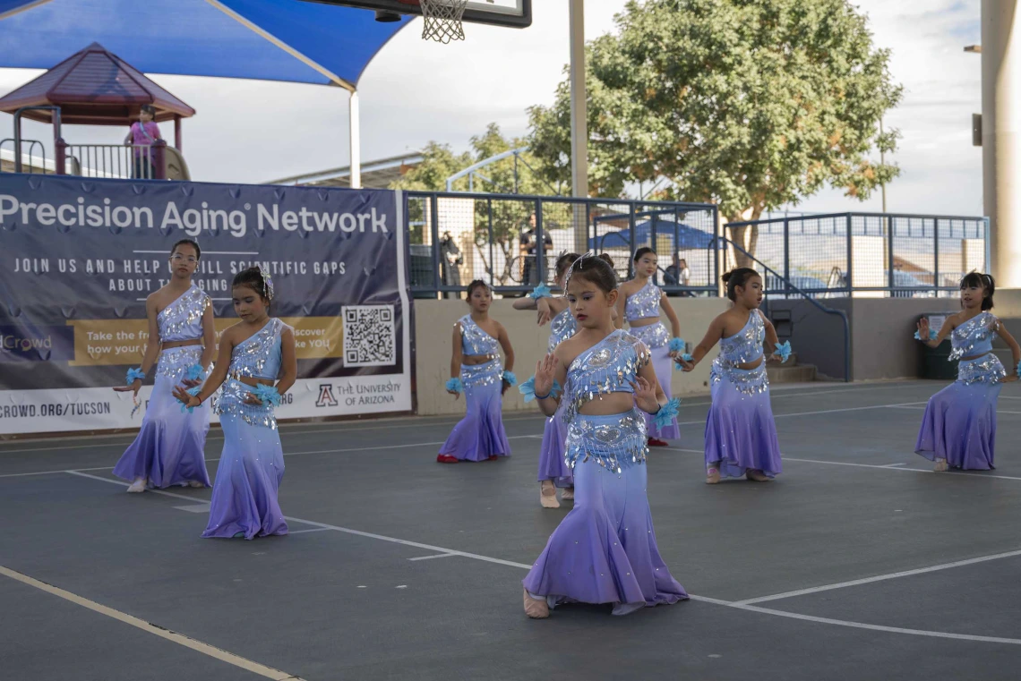 Several young dancers in dresses perform in an outdoor setting. 