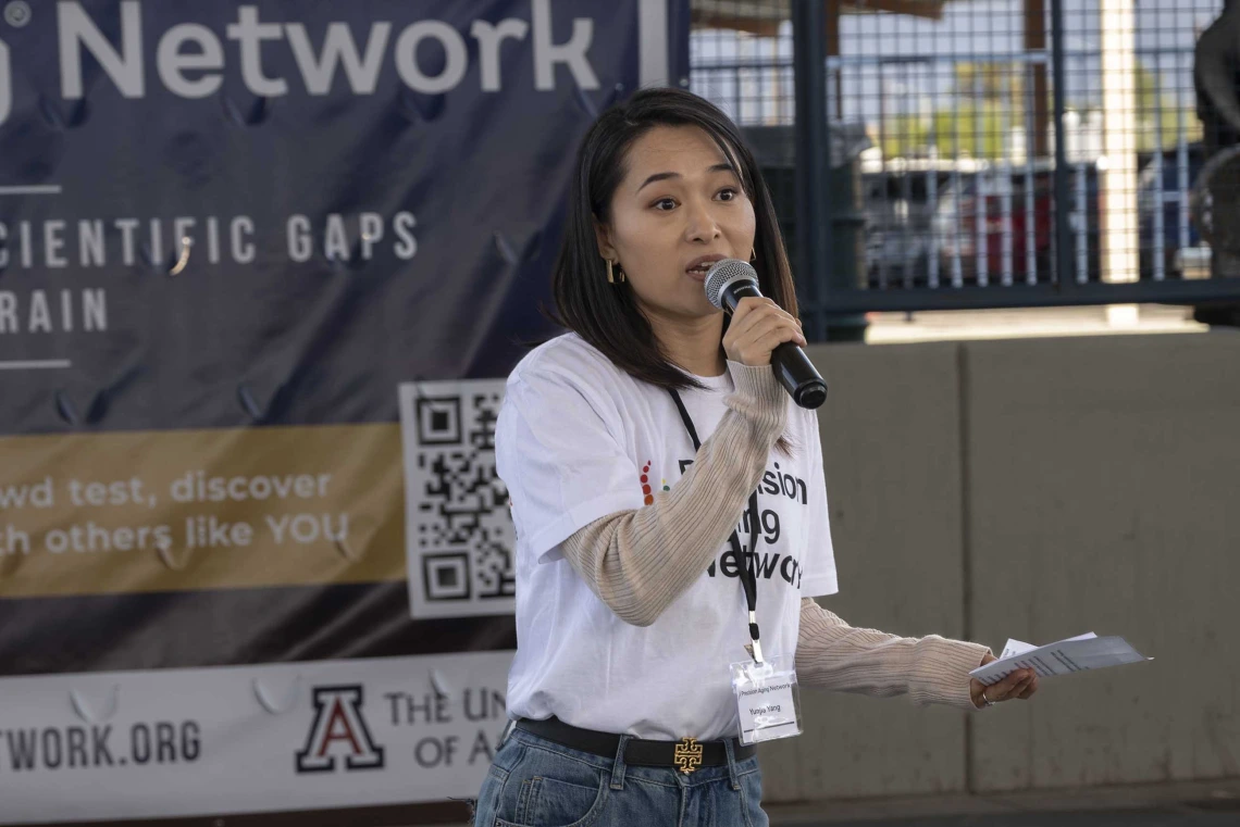 A woman in a white shirt speaks into a microphone. 