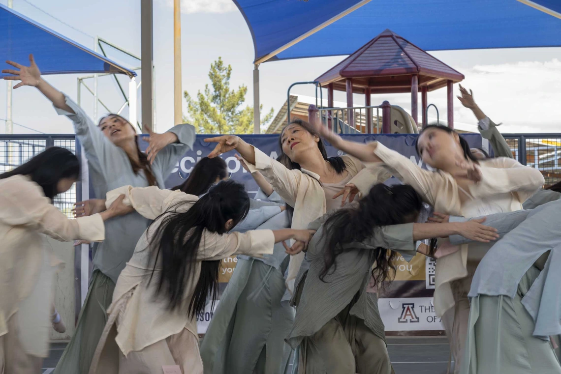 Several dancers in neutral-colored flowing clothes lift their arms and bend their bodies during a dance. 