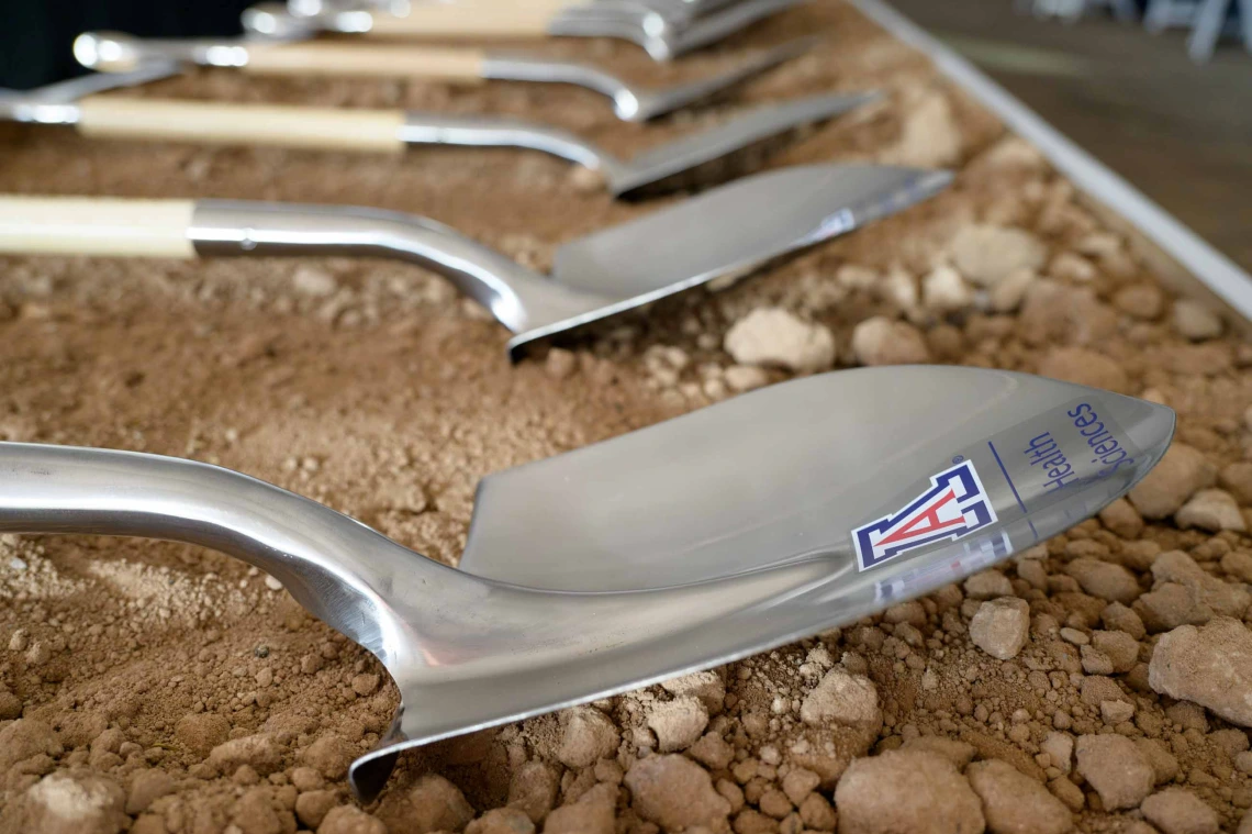 Several silver shovels with the University of Arizona logo on them lay in the dirt. 