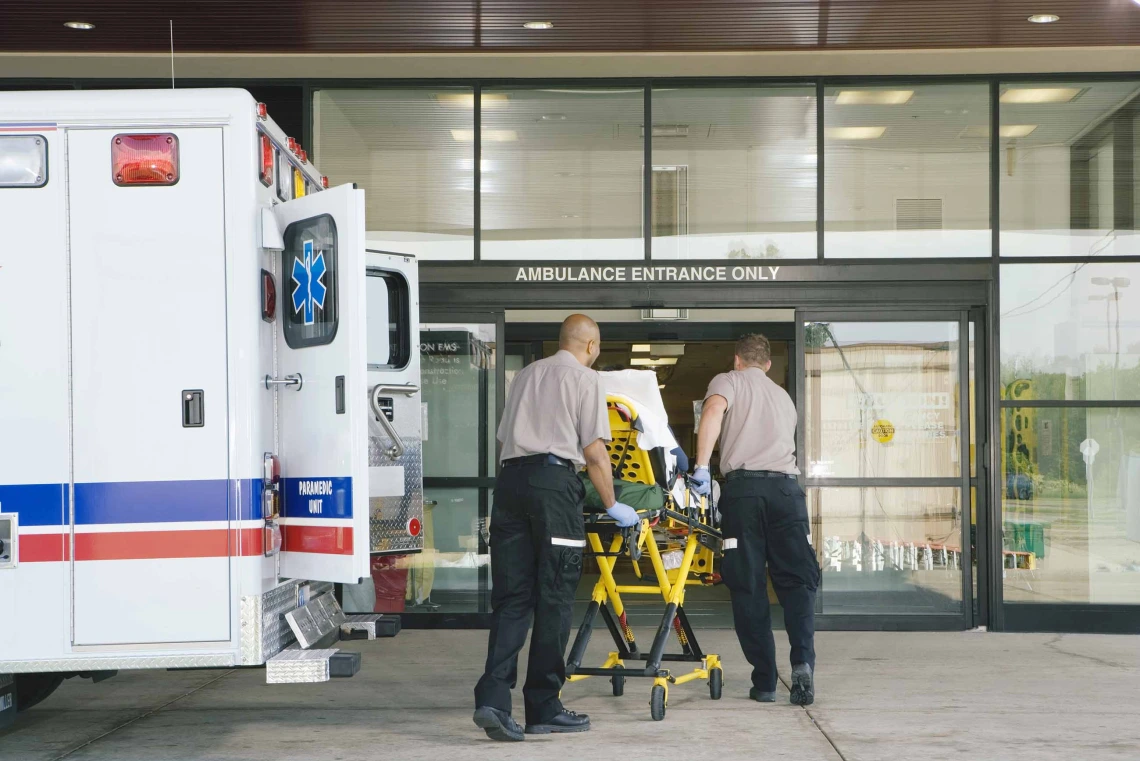 Paramedics move a patient on a stretcher from an ambulance into a hospital.