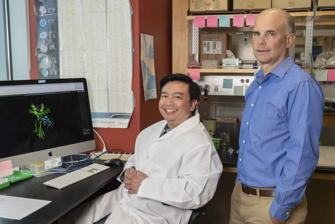 Two immunologists, one seated and one standing, pose in a University of Arizona Health Sciences research laboratory