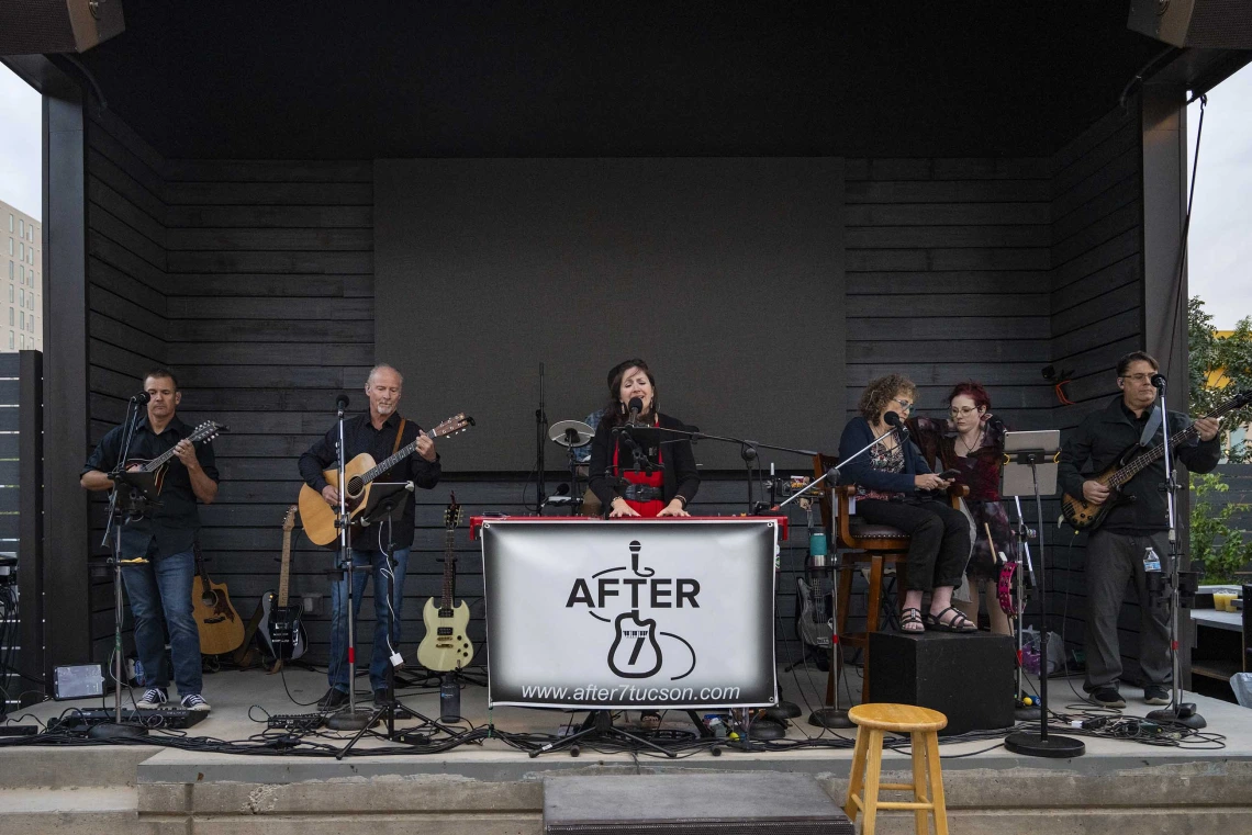 Photo of a line of musicians outside on a stage with a logo reading the band’s name, After 7.