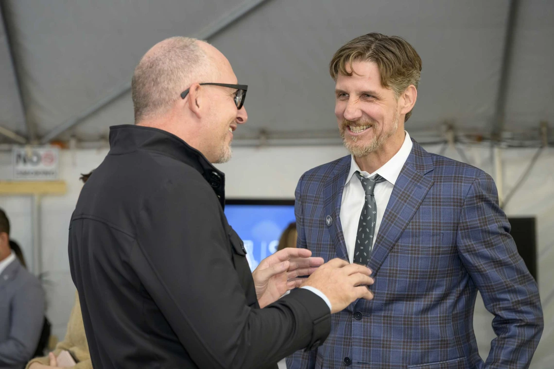 Two smiling men in dark coats face each other as they talk.