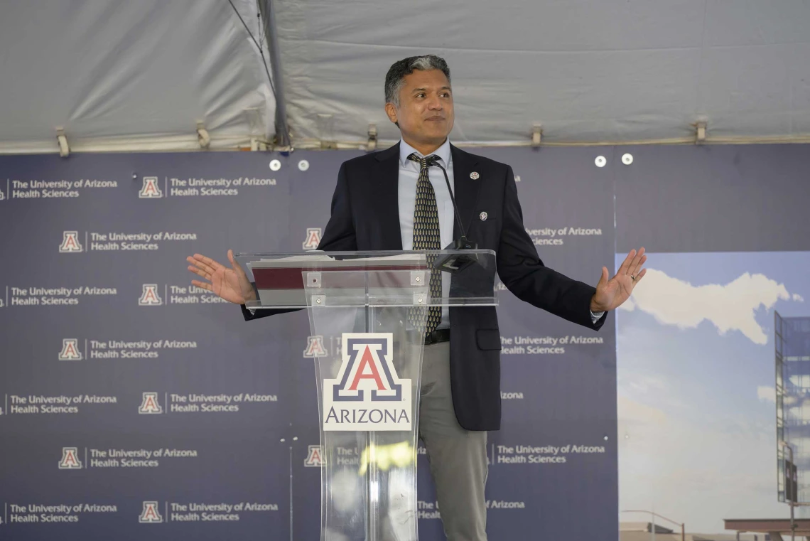 Deepta Bhattacharya, PhD, inaugural executive director of CAMI and a professor of immunobiology at the U of A College of Medicine – Tucson, wearing a dark suit, stands behind a clear lectern with the U of A logo on it.  