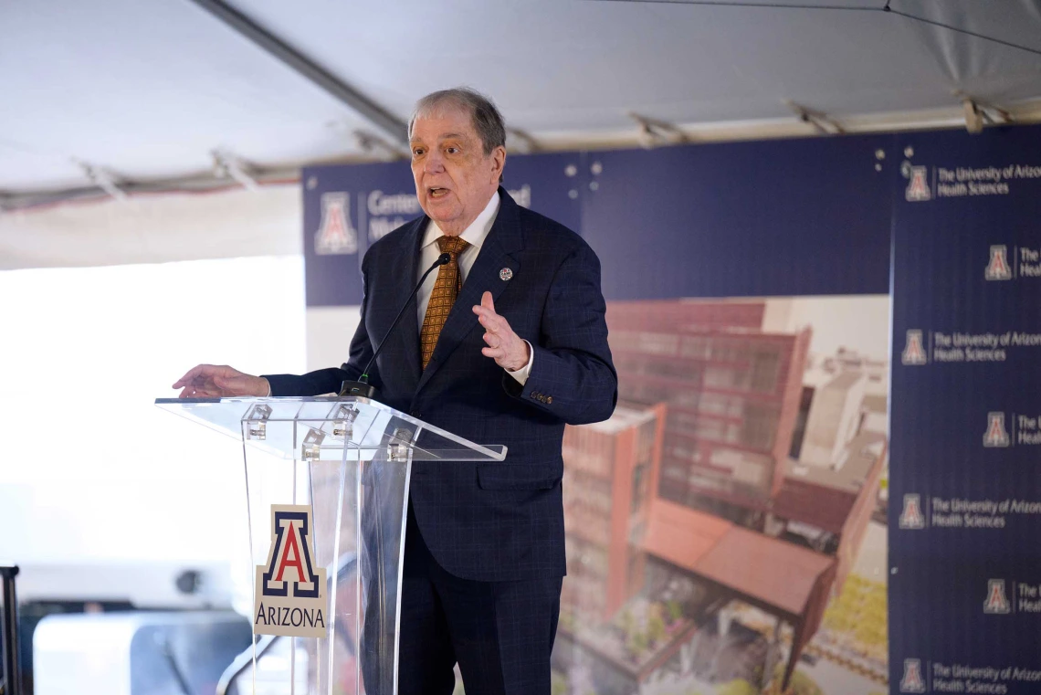 Michael D. Dake, MD, senior vice president for the University of Arizona Health Sciences, wearing a dark suit, stands on a stage at a clear lectern with the U of A logo on it.  