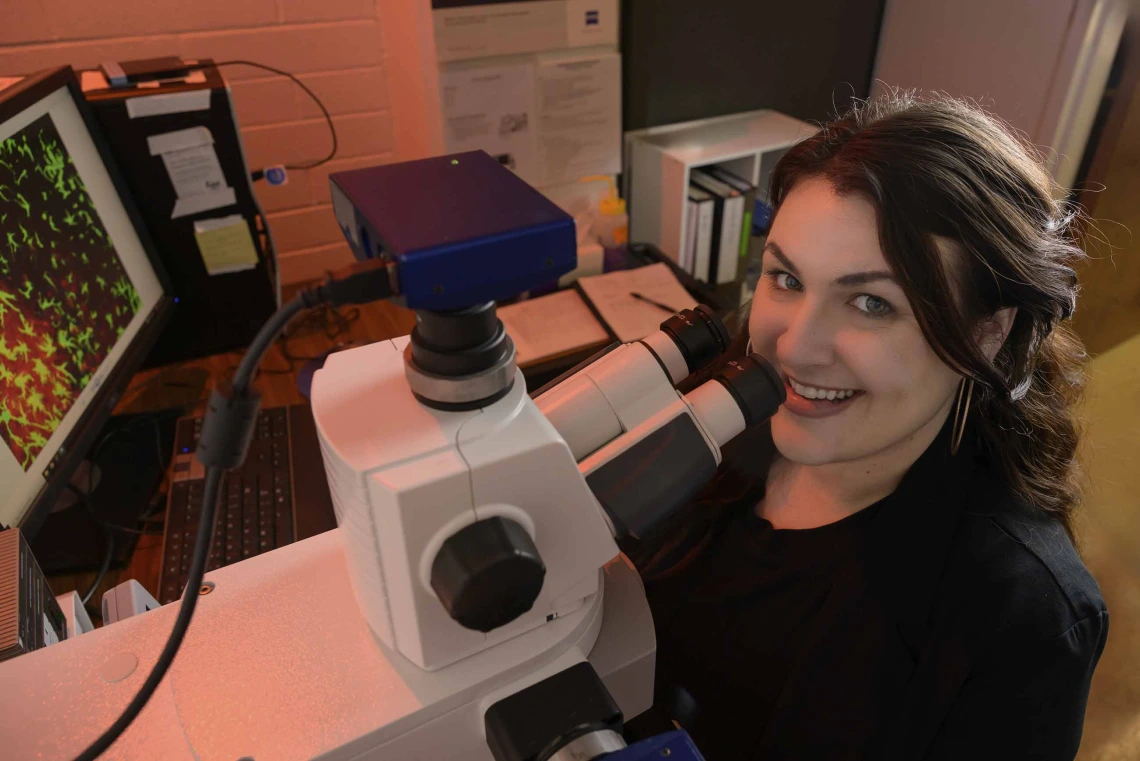 Portrait of a woman looking up from a microscope and smiling.