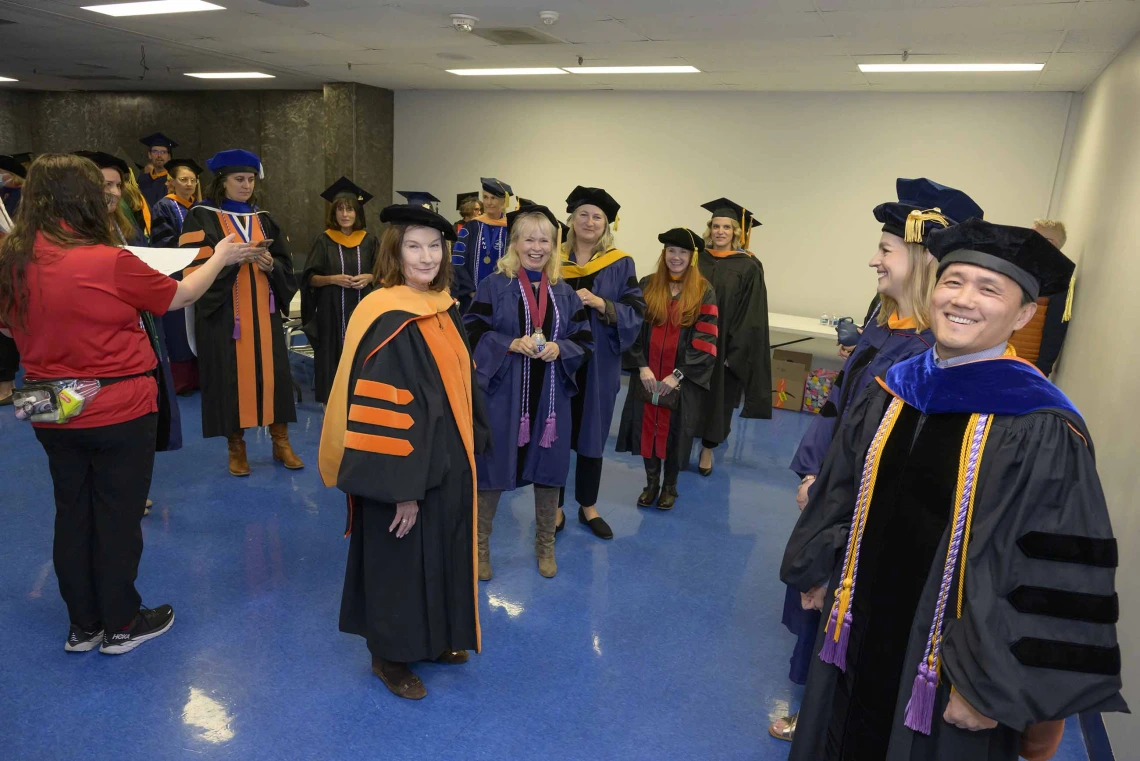 More than a dozen University of Arizona College of Nursing faculty and staff members dressed in graduation regalia smile as they line up in a room.