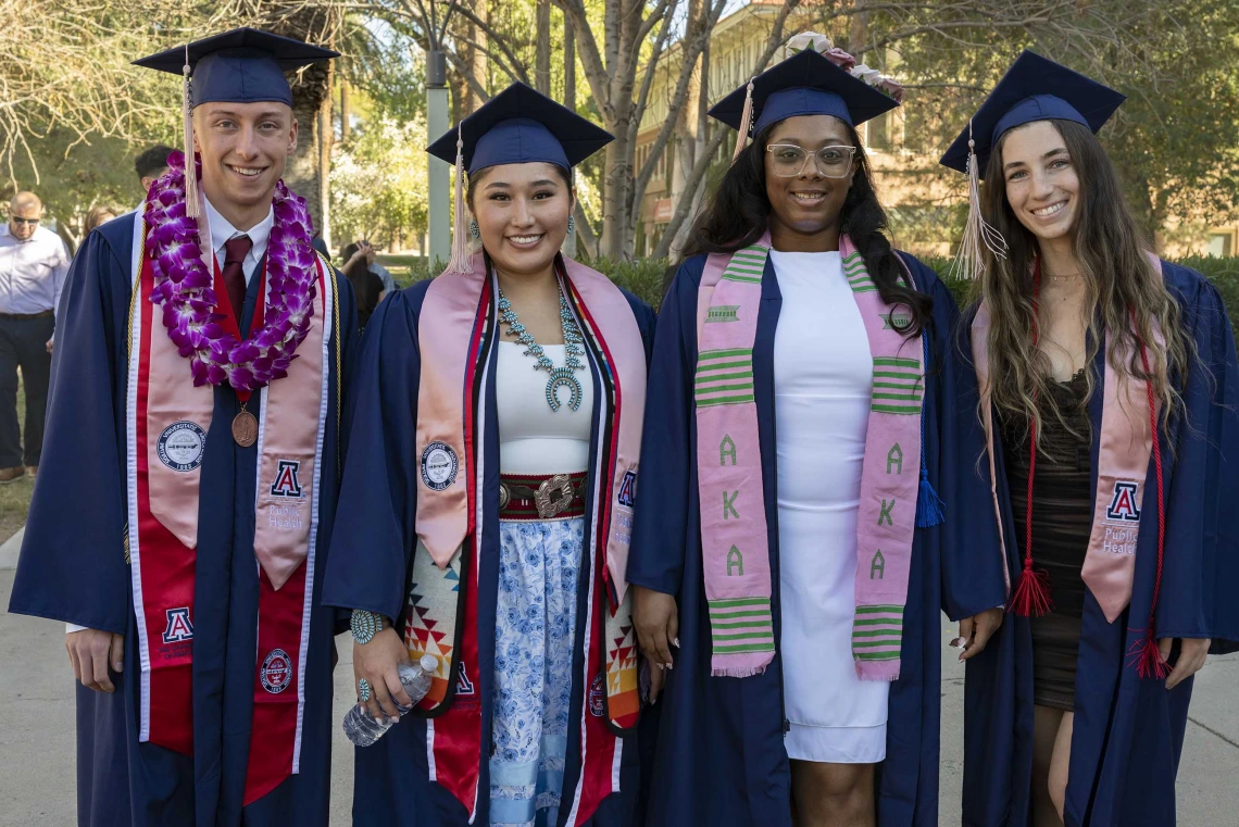 Four University of Arizona Mel and Enid Zuckerman College of Public Health students stand together wearing graduation caps and gowns.  