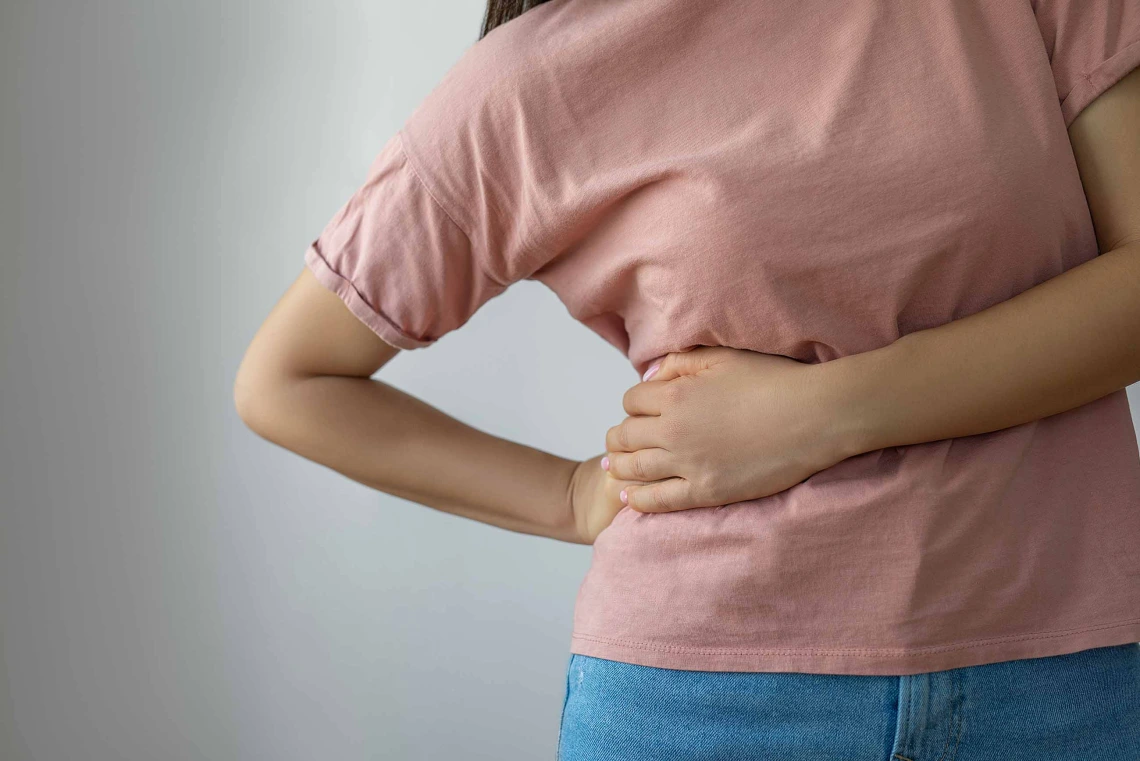 A woman grabs at the right side of her torso with both hands in a gesture of pain.