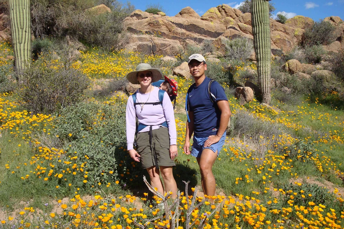 A couple with a baby in a carrier poses for a photo while hiking in the Sonoran Desert