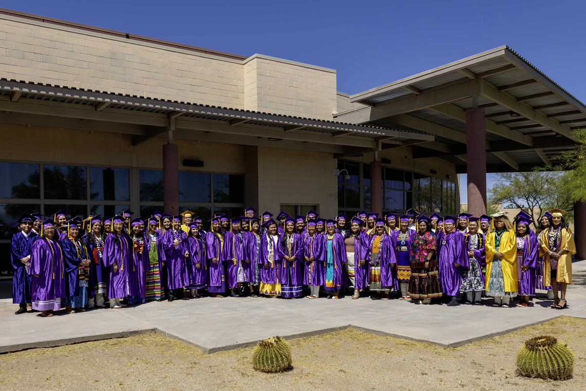 Graduates of the Tohono O’odham Community College Class of 2024 pose for a photo outside the college on a sunny day.