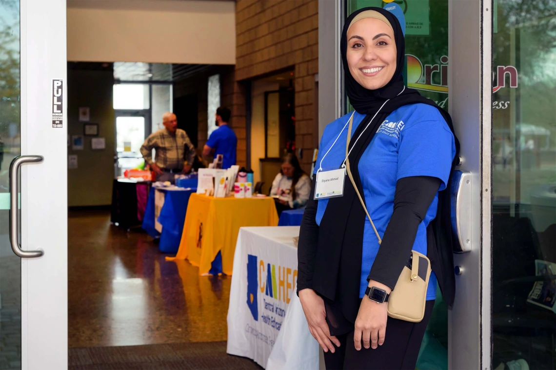 Arizona AHEC Scholar Diyana Ahmad smiles and holds the door open for people to enter community health clinic in Apache Junction, Arizona  