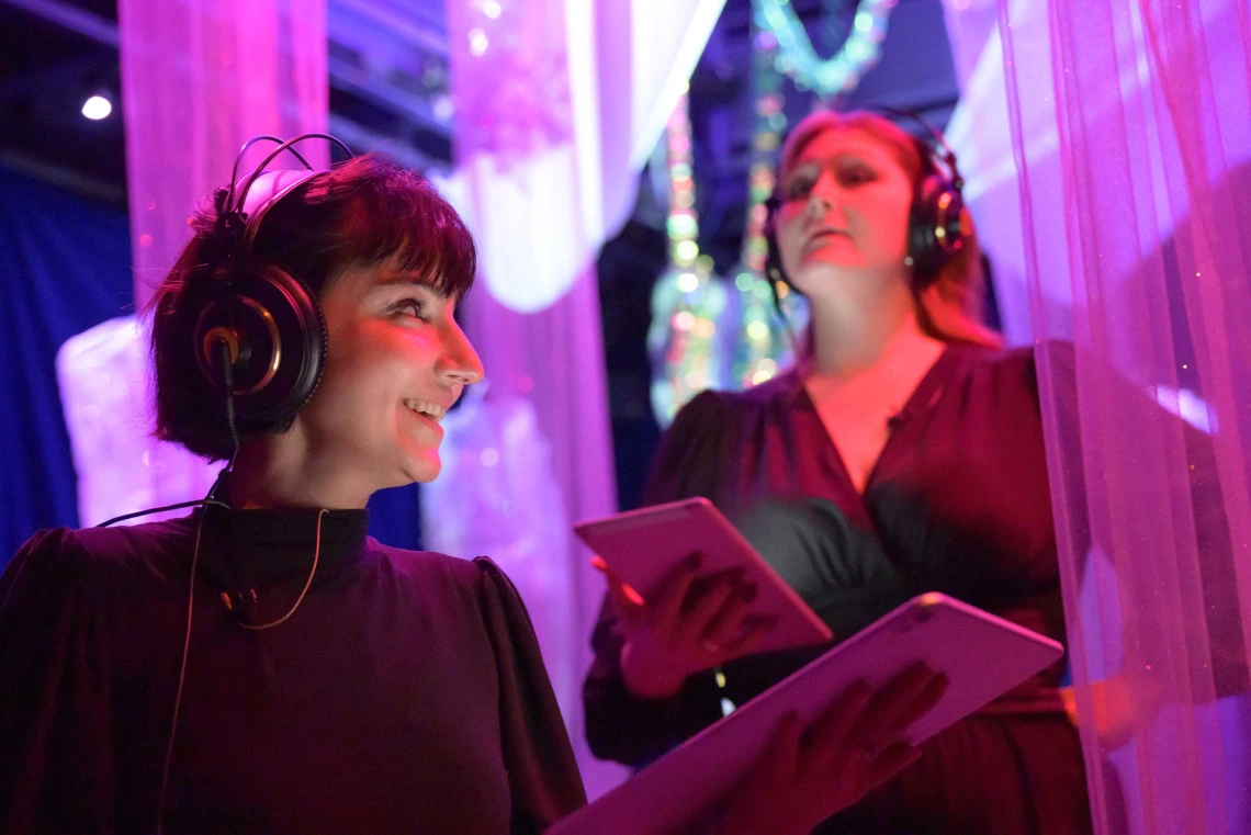 Two singers wearing headphones and reading music on a tablet