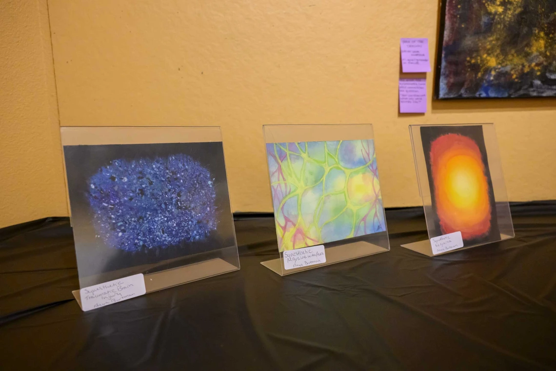 Three pieces of colorful artwork are displayed on a tabletop with a black tablecloth