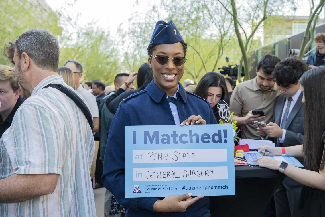 A woman wearing a blue Air Force uniform and sunglasses smiles as she holds up a sign that reads, “I Matched!”