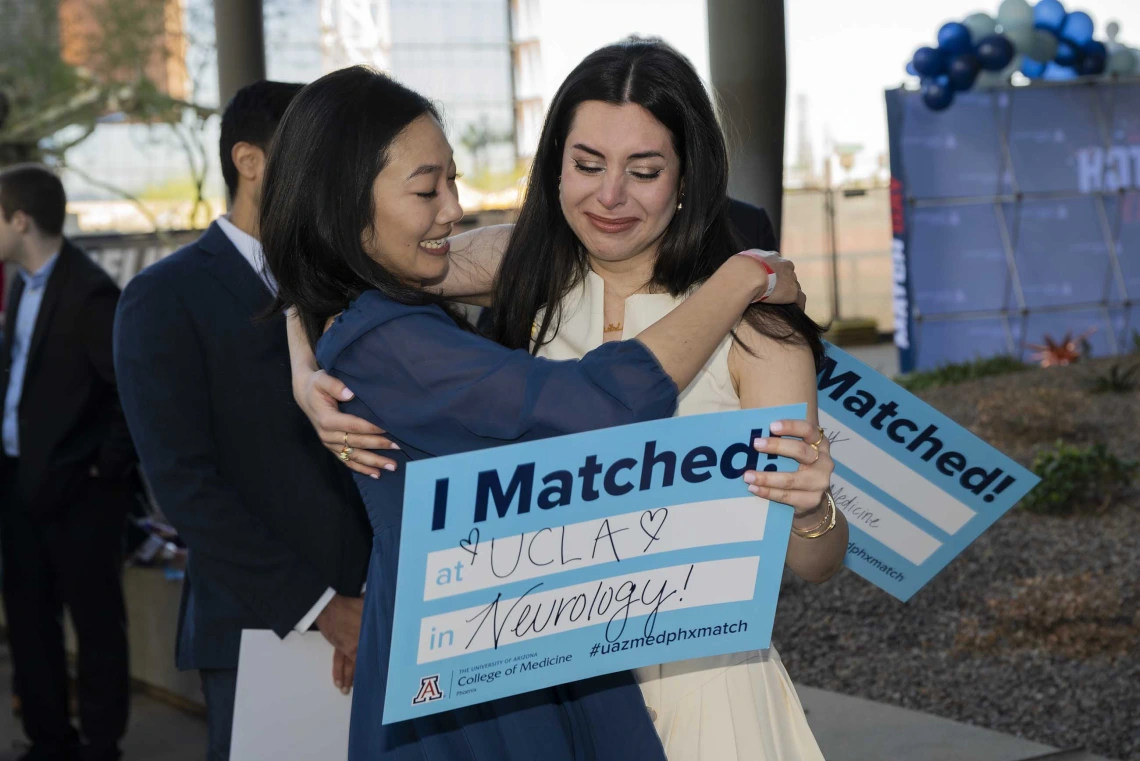 Two young women hug and smile as they hold signs that read, “I matched!”