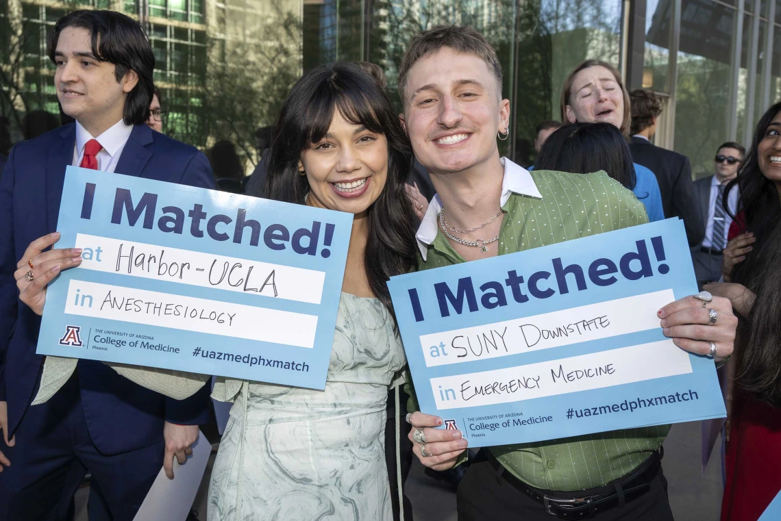 A woman and man both smile as they hold up signs that read, “I Matched!”