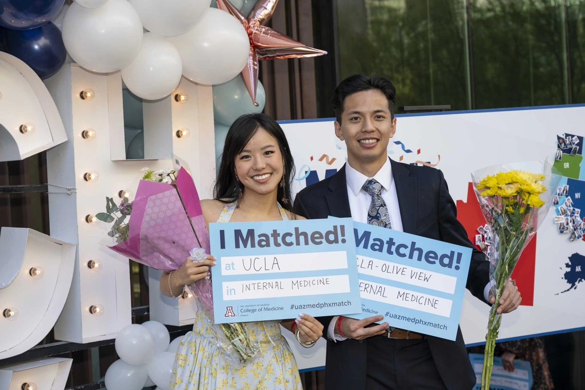 A woman and man both smile as they hold up signs that read, “I Matched!”