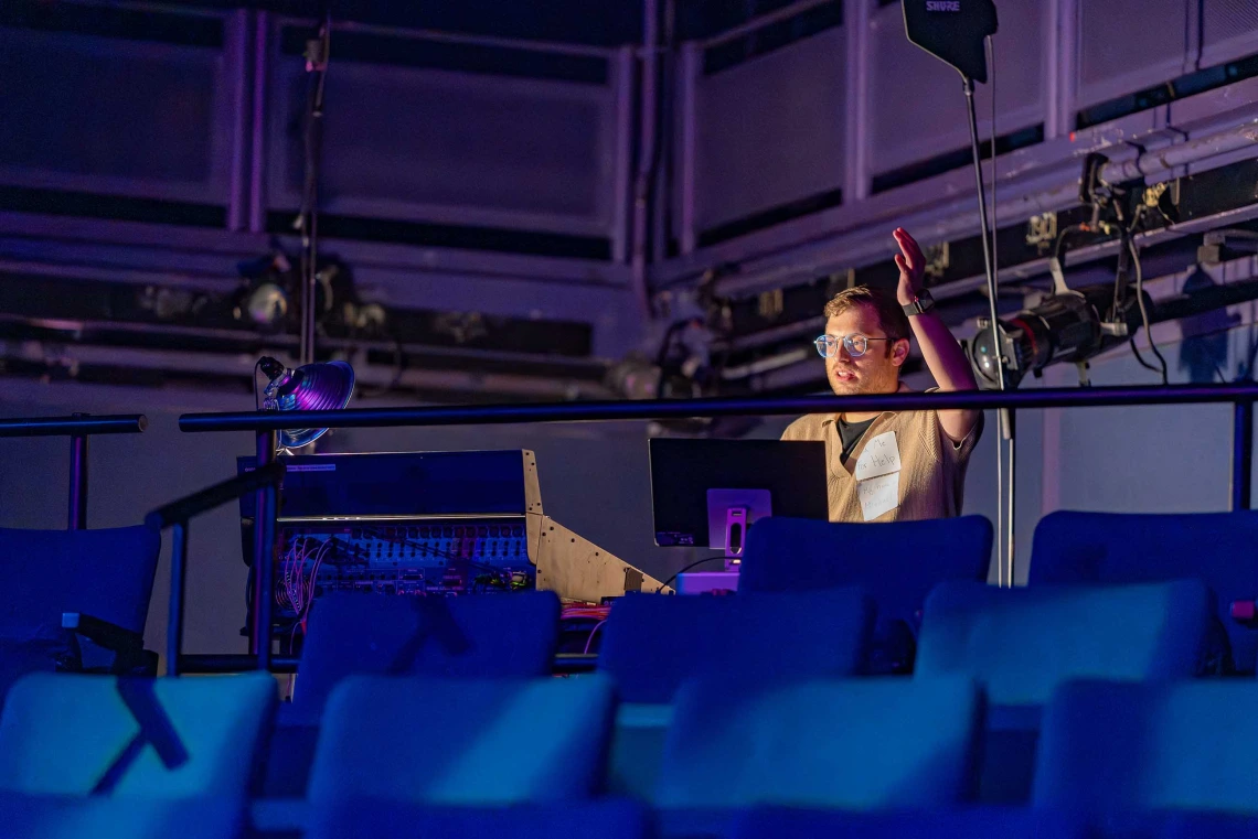 Person conducting singers from a sound booth in the searing area at the Tornabene Theater