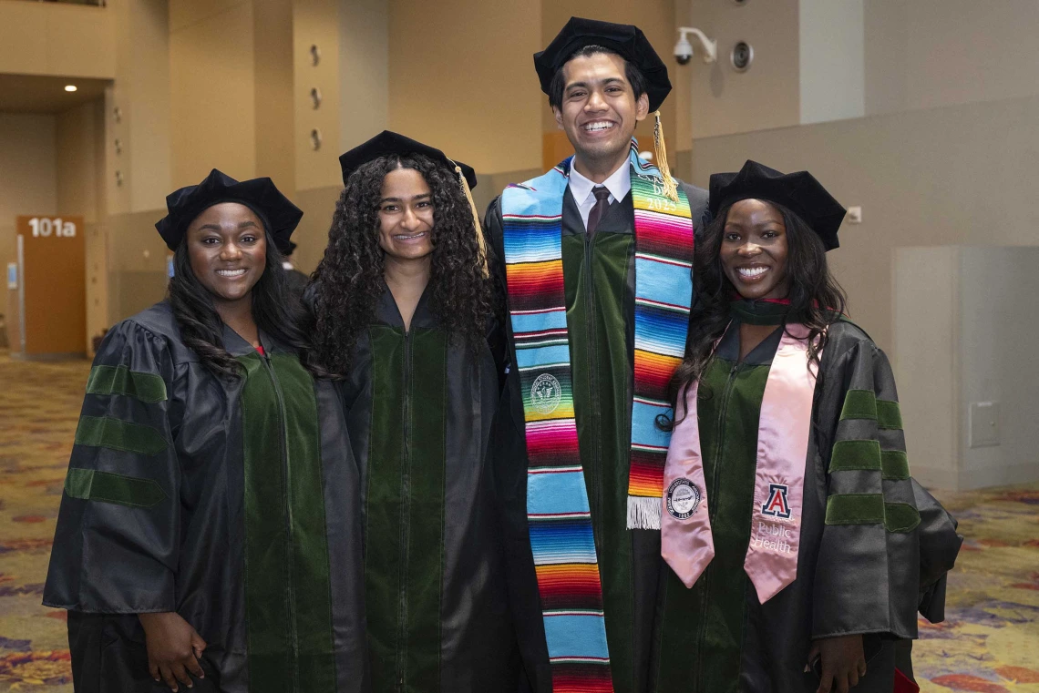 Four medical students stand together, smiling, in their graduation caps and gowns. 