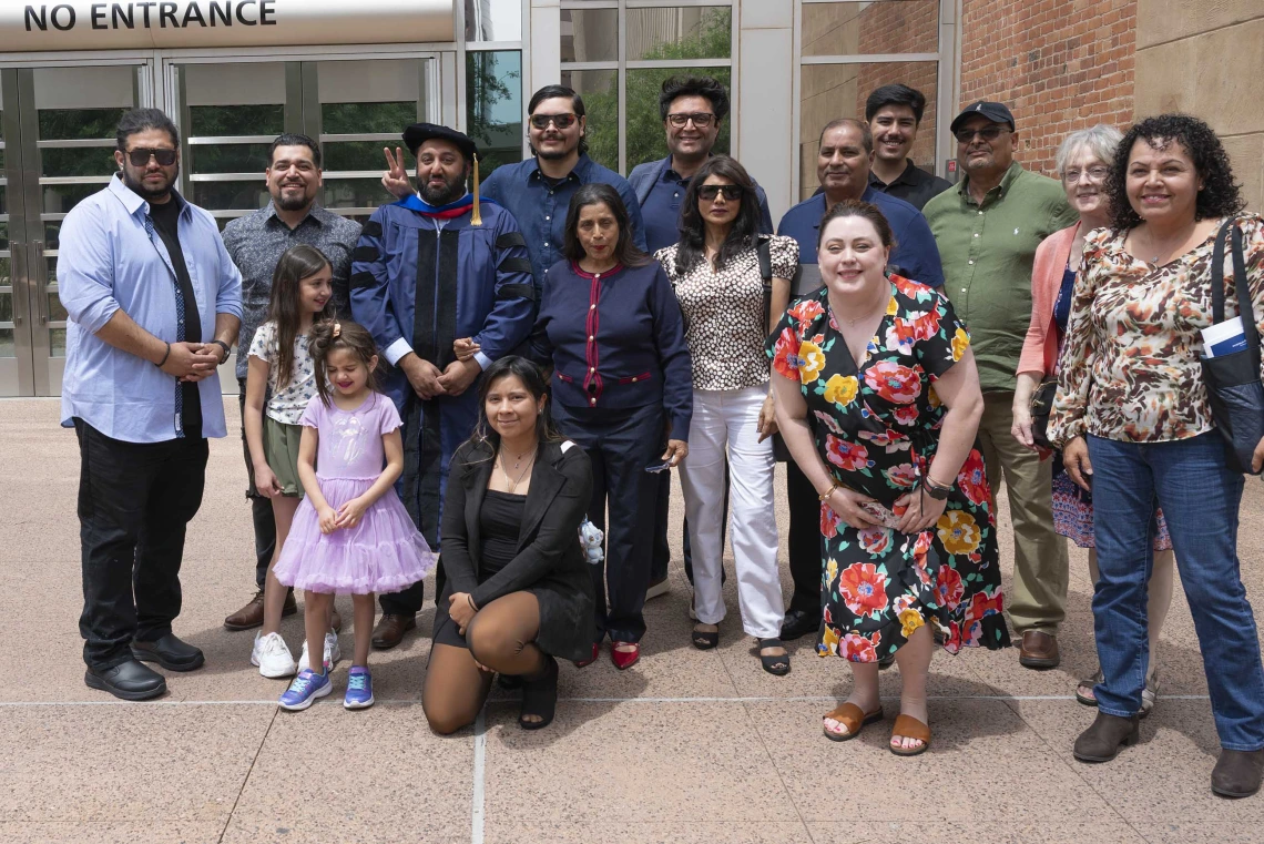 A graduate wearing a cap and gown stands in the middle of over a dozen family members of all ages. 