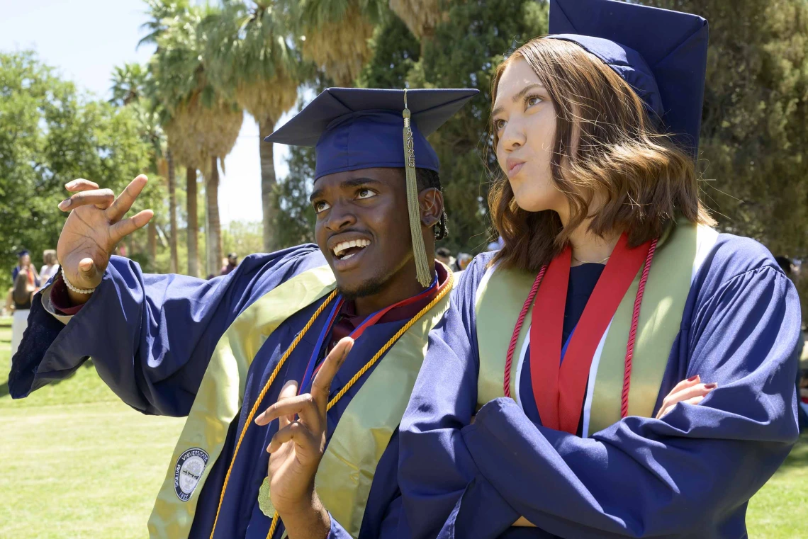 A young man and woman in graduation caps and gowns make silly faces and look as if they are pondering their futures. 