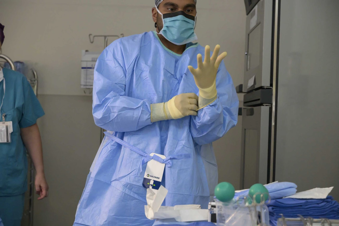 Health care worker in mask and surgical gown putting on a glove
