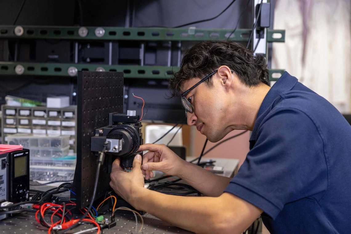 A researcher is hunched over an imaging device that he is working on in a laboratory.