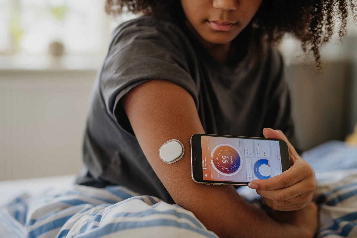 Young adult connecting smartphone to continuous glucose monitor, checking blood glucose