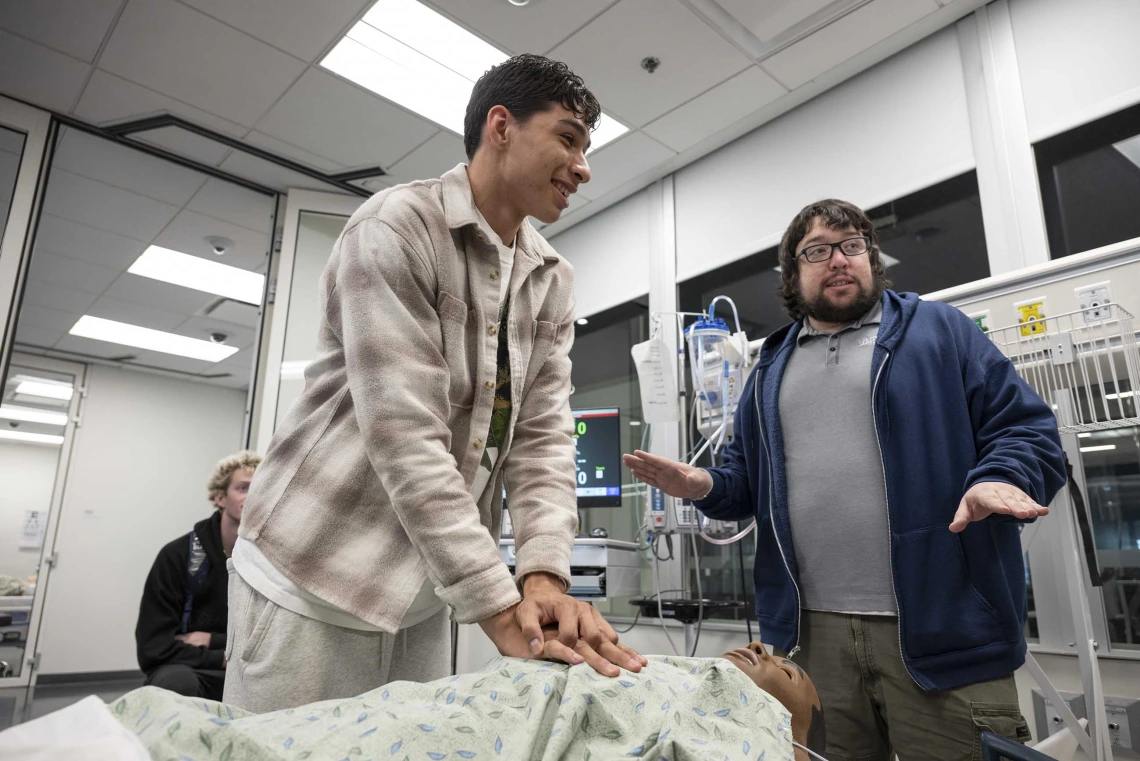 A high school student practices chest compression on a manikin while an instructor offers advice. 