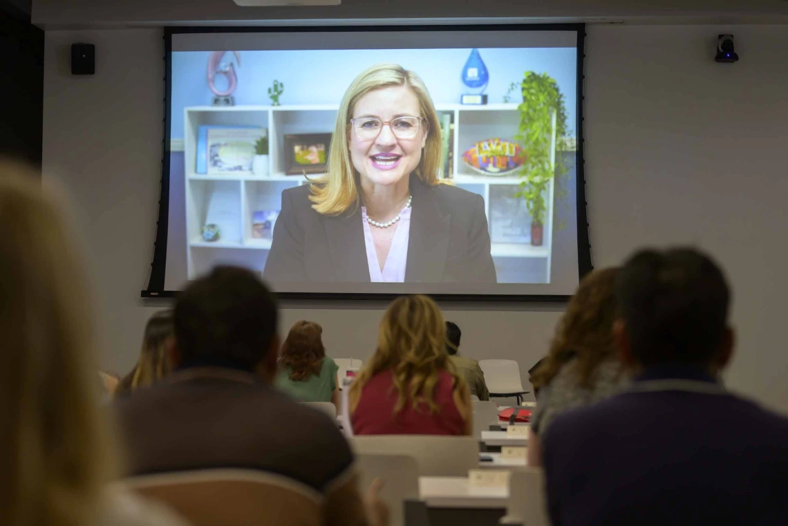 A large projector screen in a spacious conference room at the Phoenix Bioscience Core displays a recorded video message from Phoenix Mayor Kate Gallego, addressing rows of seated educators. 