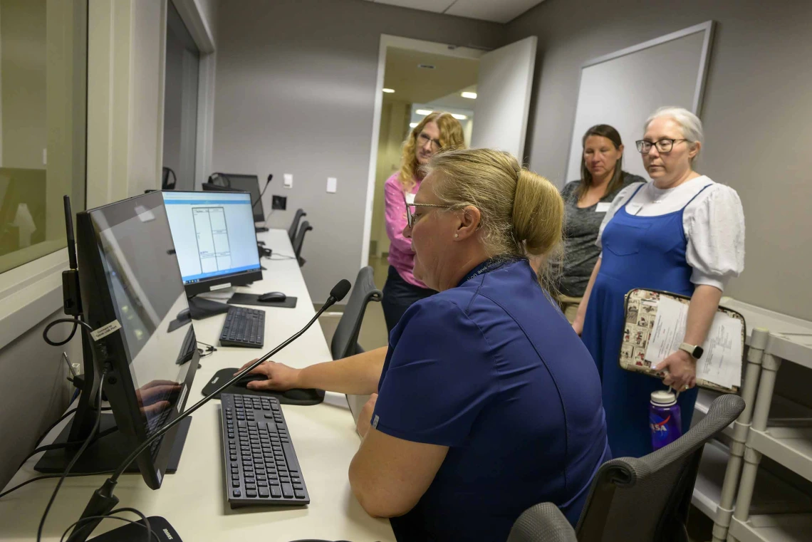 A woman sits at a control desk with multiple monitors and controls in the Center for Simulation and Innovation at the University of Arizona College of Medicine – Phoenix, managing a health care simulation.