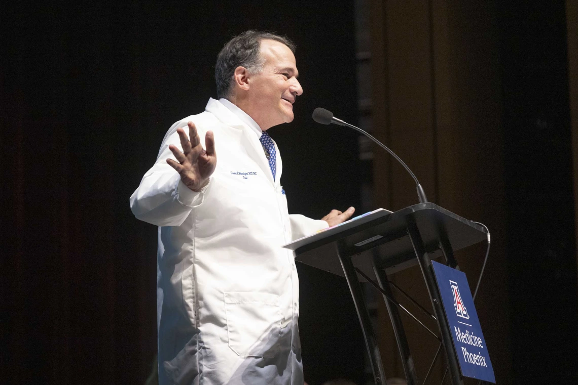 Fred E. Wondisford, MD, MS, MBA, speaks at a lectern while wearing a medical white coat. 
