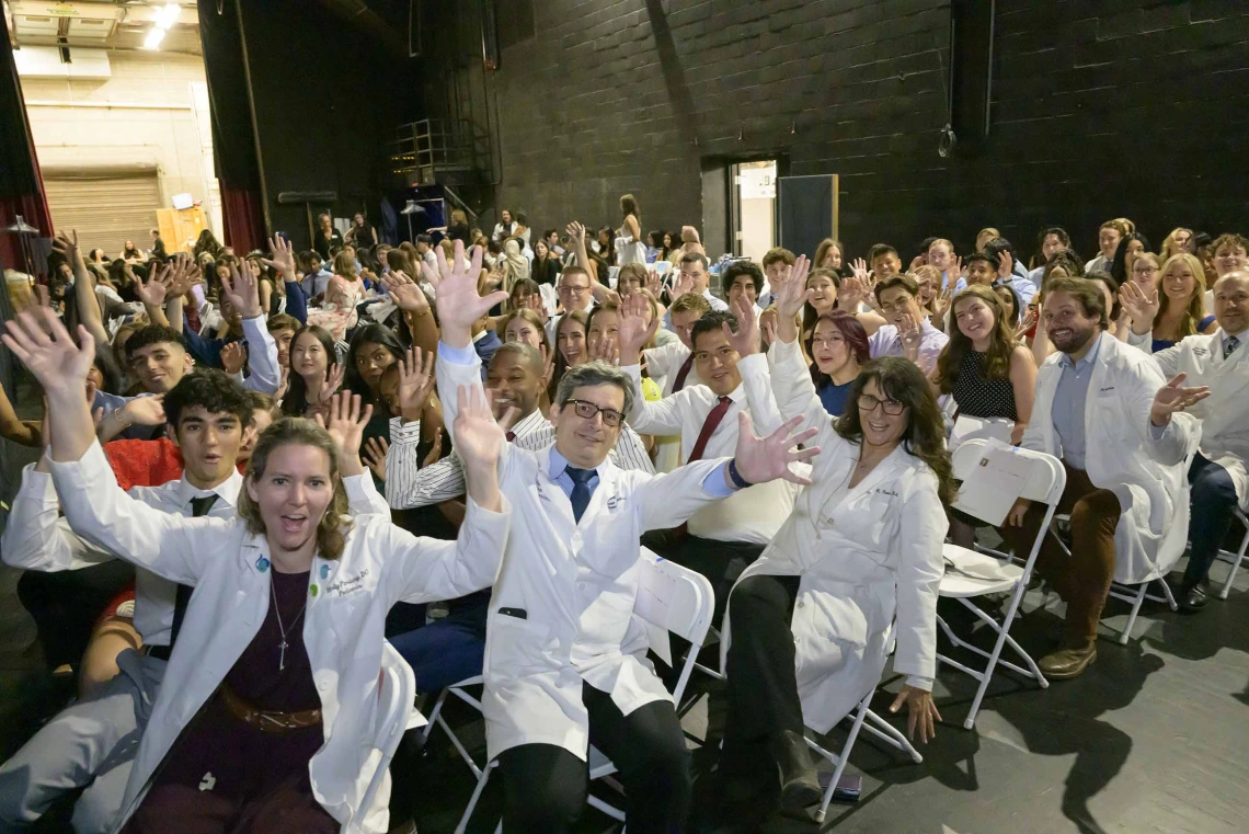 More than 100 U of A College of Medicine – Tucson professors and first-year medical students wave as they wait in chairs backstage at Centennial Hall. 