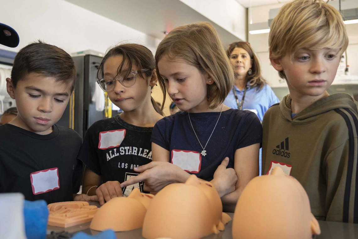 Four elementary students look at silicone faces on a table. 