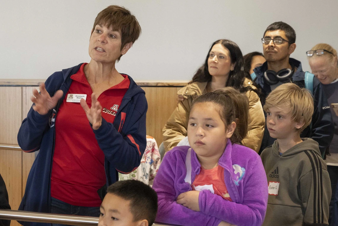 A woman in a red University of Arizona shirt talks to a group of elementary students. 