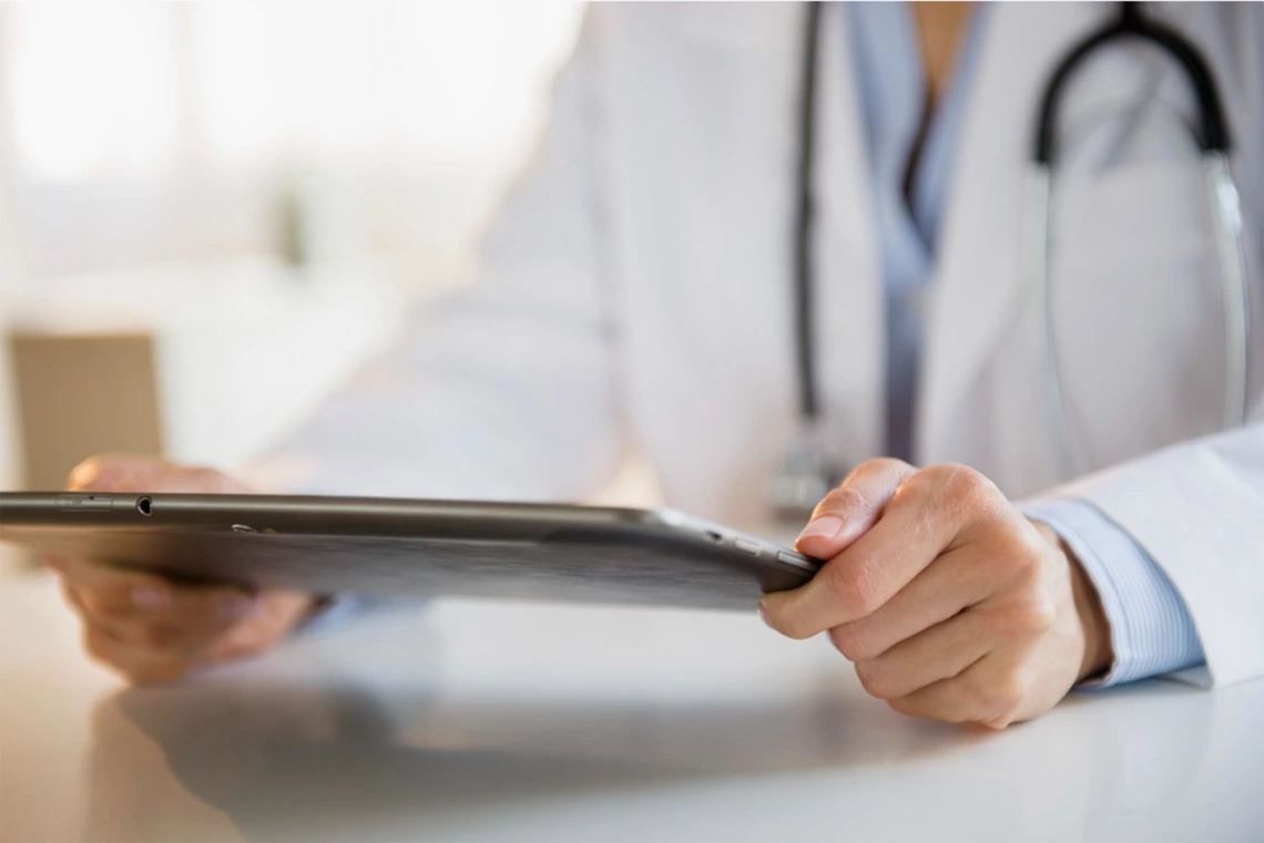 close up of doctor wearing white coat and stethoscope around neck holding an ipad