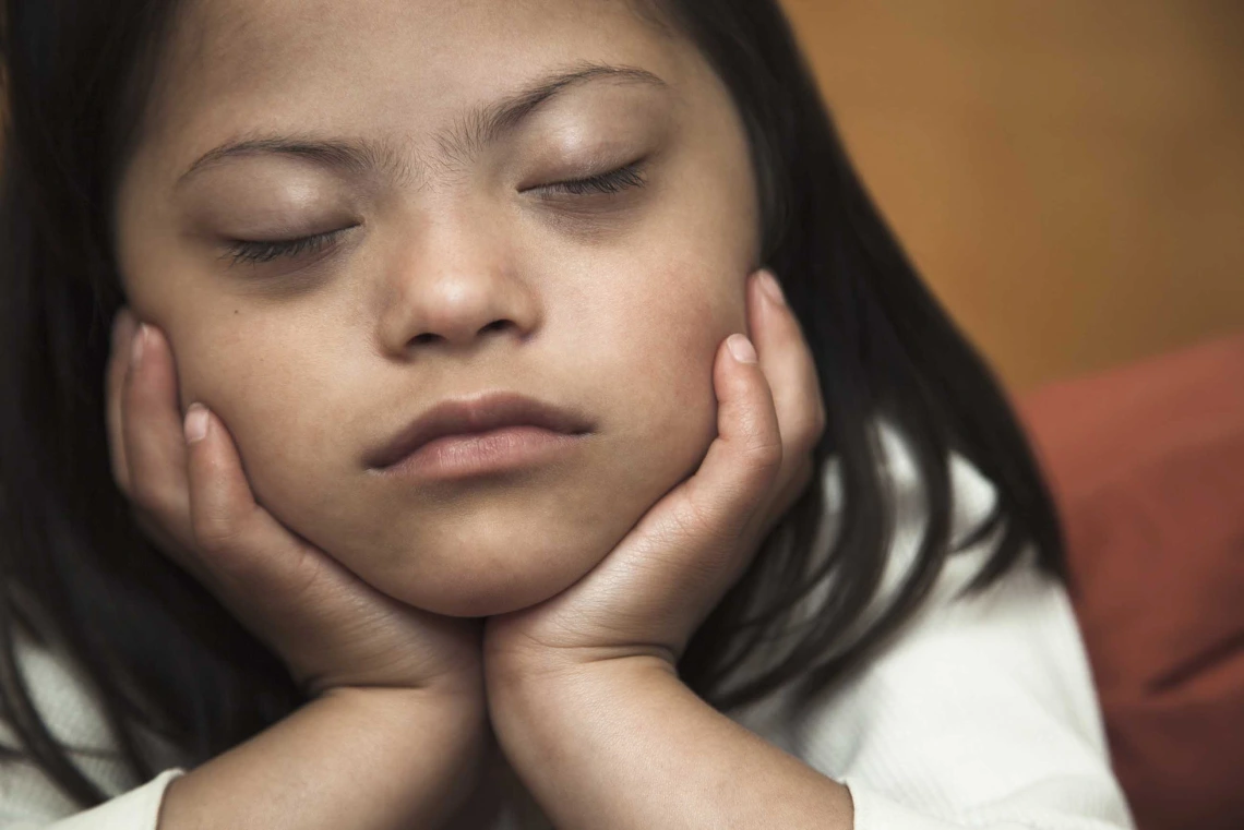 A girl with eyes closed and her chin resting in her hands