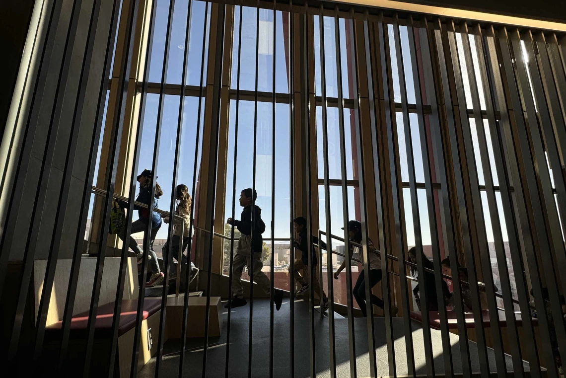 Students walk up stairs behind a dark vertical line barrier with a blue sky behind them. 