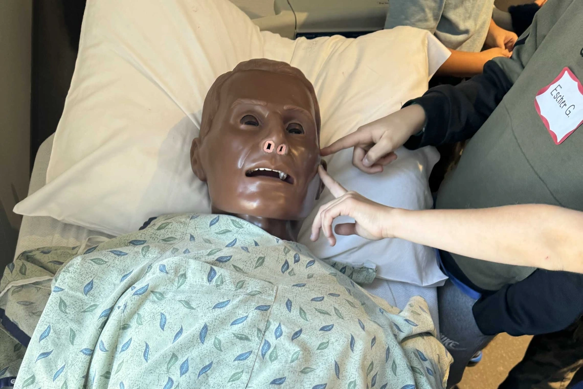Hands reach out to touch a plastic manikin wearing a hospital gown. 