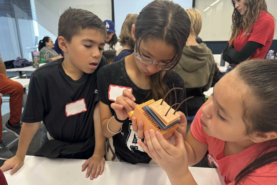 Elementary students stand around a table assembling a 3-D puzzle of the layers of human skin. 