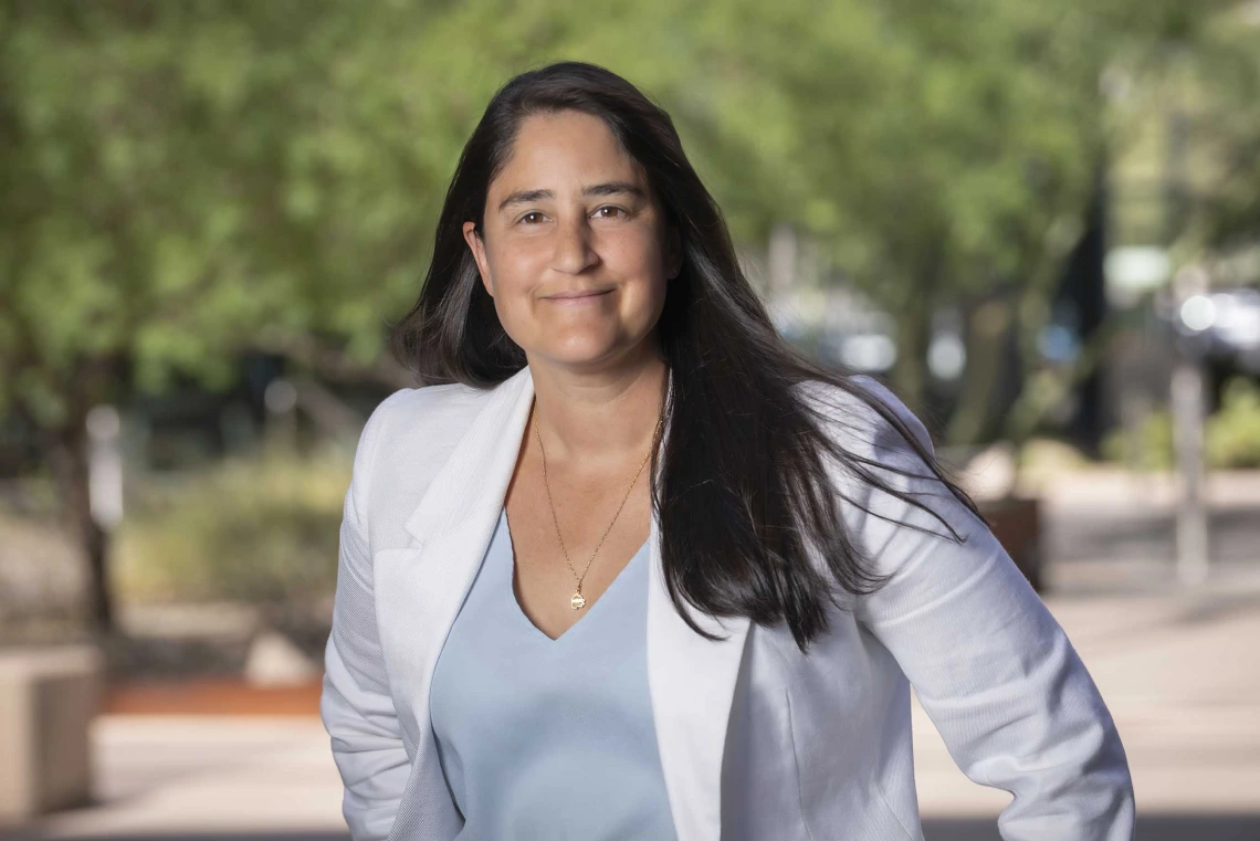 Portrait of Maya Kaelberer wearing a white blazer in an outdoor setting with trees in the background