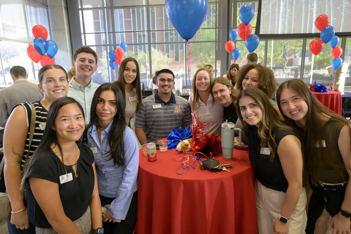 Several people look at the camera smiling with red and blue balloons in the background.