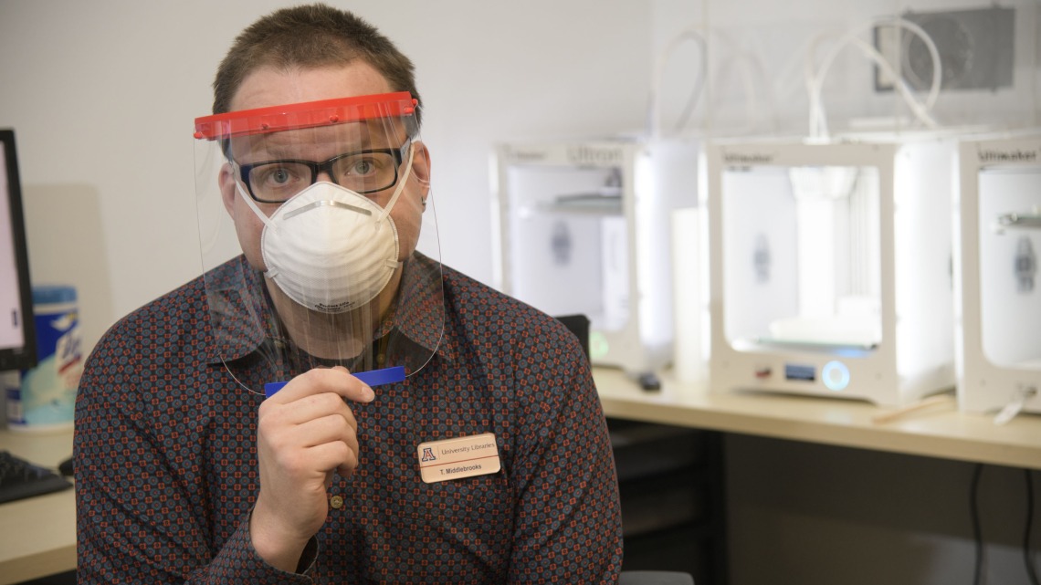 Tory Middlebrooks, of University Libraries, models a face shield, which is designed to be worn in conjunction with additional PPE such as a mask. Middlebrooks mans the 3D printers that produced the headbands for the face shield.