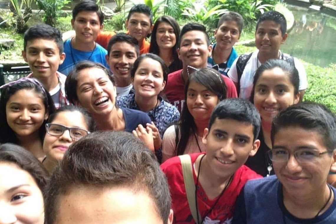 Large group of middle school-aged kids gather around for a selfie in a lush and tropical environment