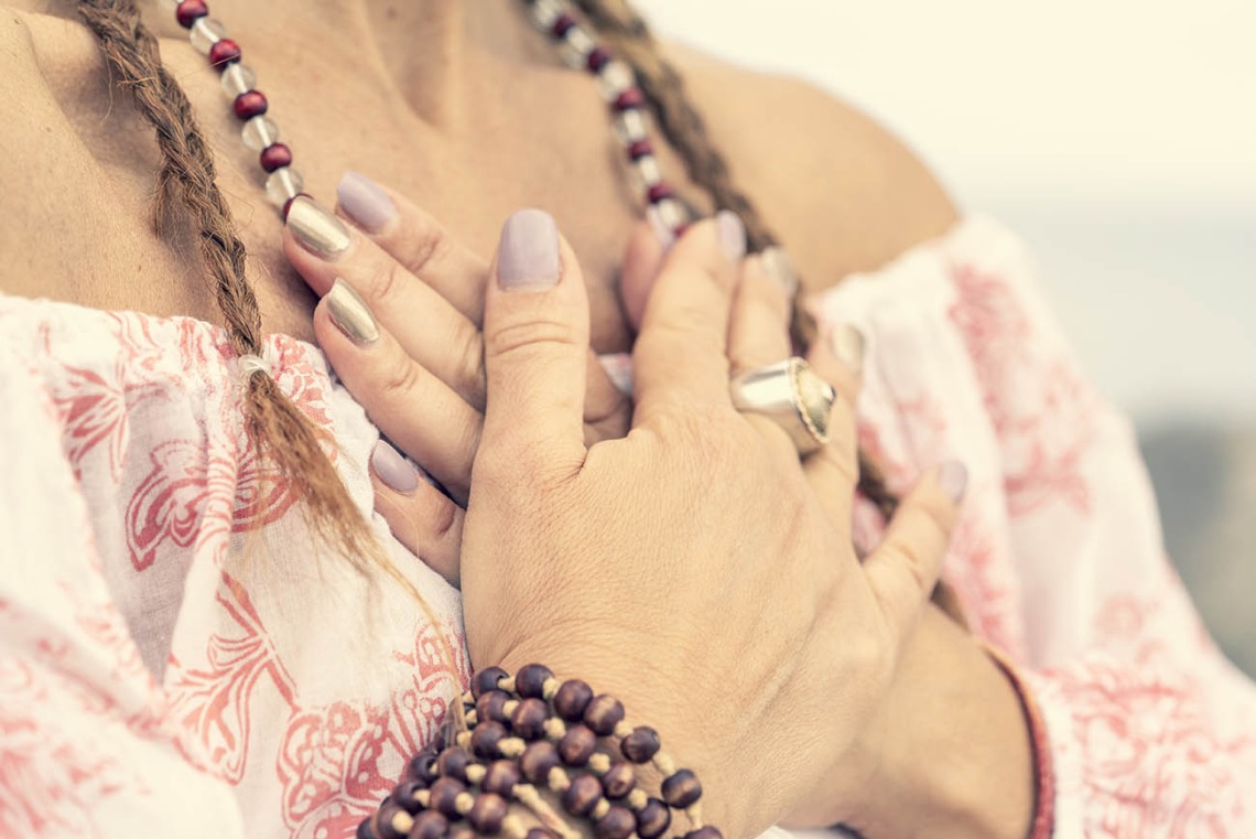 Woman with purple nails and rings covers her chest with her hands