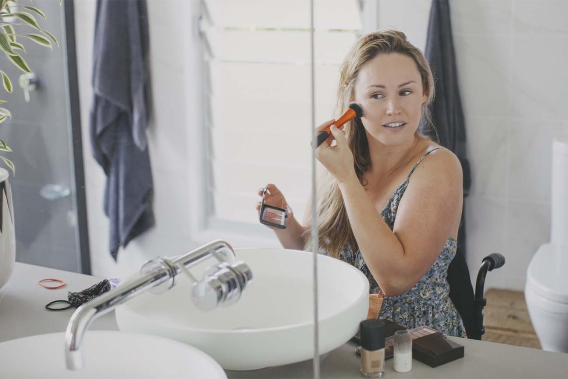Paraplegic woman applying makeup in bathroom mirror