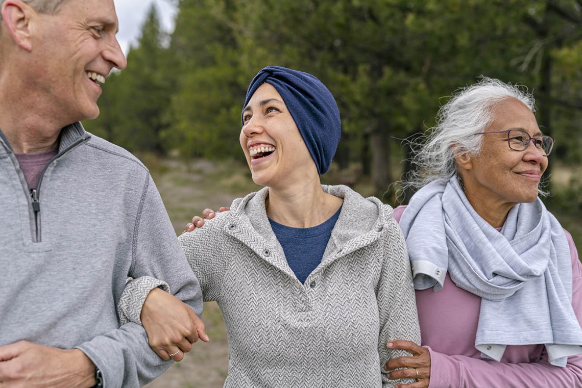 Woman in a gray sweatshirt and blue headscarf links arms with two older adults
